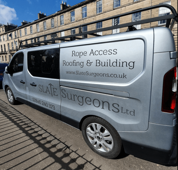 A grey van belonging to Slate Surgeons Ltd, displaying services such as Rope Access, Roofing & Building, with the website URL and contact number visible.